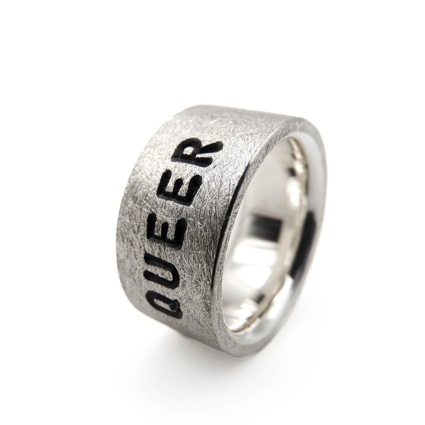 Nahaufnahme der Gravur „Queer“ auf einem 925er Silberring für die 
Pride-Community, eismatte Oberfläche