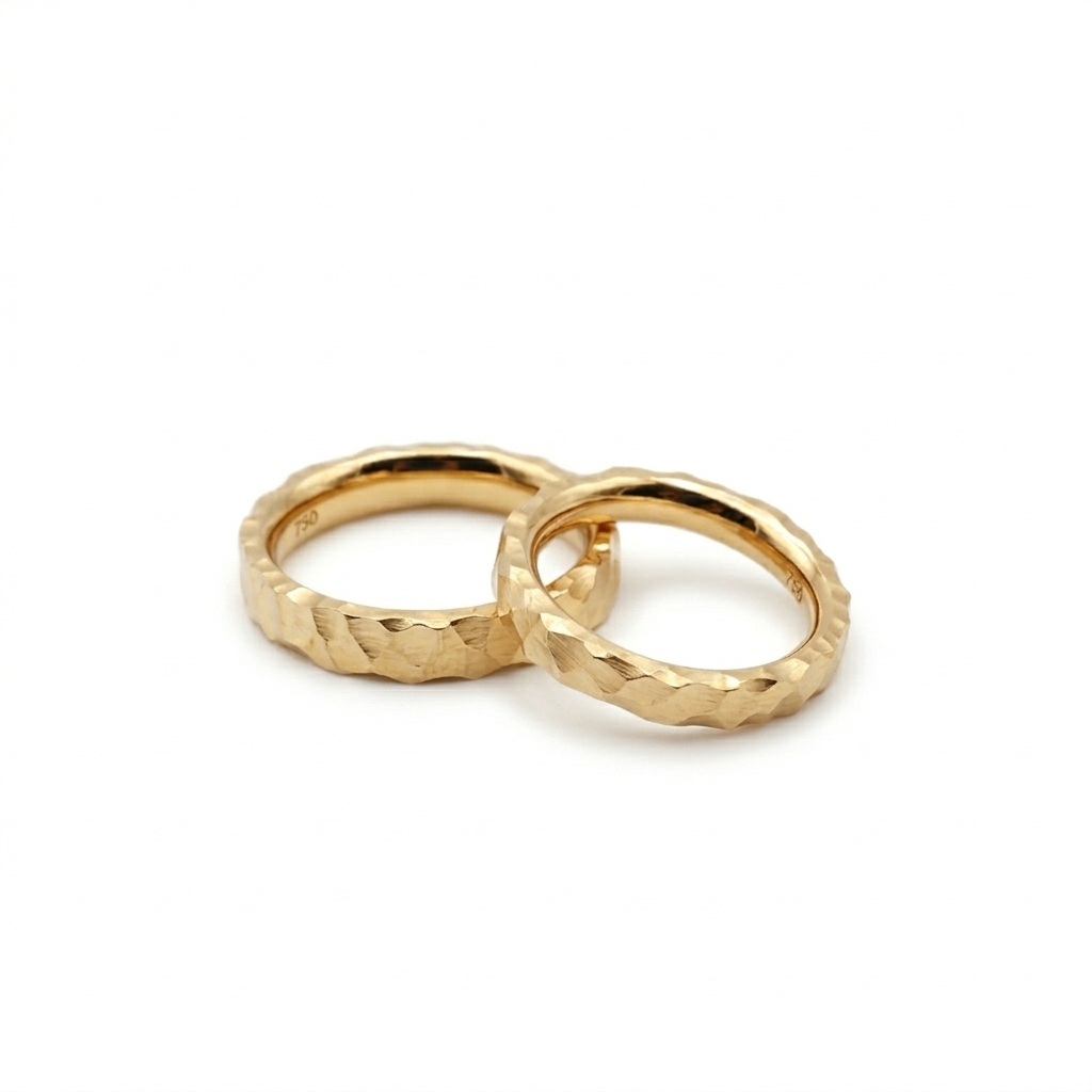 Zwei personalisierbare Trauringe aus massivem Gold mit markanter Hammerschlag-Optik, handgefertigt in Nürnberg.
